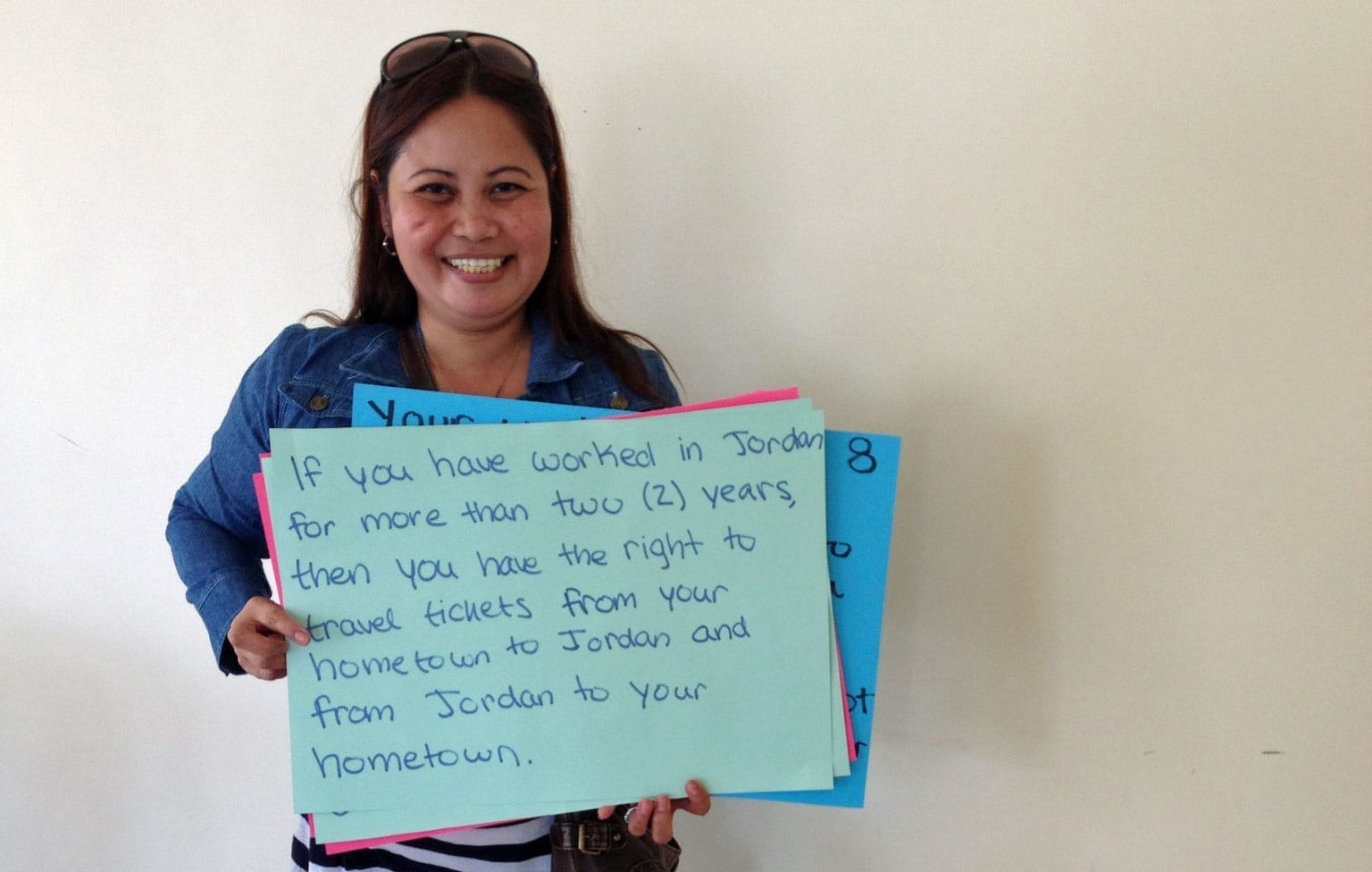 Filipina domestic worker participant, holding sign, if you have worked in Jordan for more than two years, then you have the right to travel tickets from your hometown to Jordan and from Jordan to your hometown